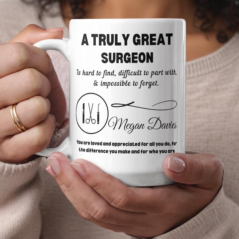 May include: White ceramic mug with the text "A Truly Great Surgeon" in black. The mug features a graphic of surgical tools and the name "Megan Davies". The mug also has a quote about surgeons.