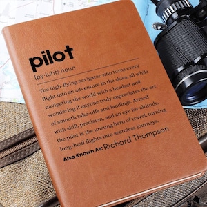 May include: A brown leather journal with the word "pilot" printed in black on the front cover. The definition of the word "pilot" is printed below the word, along with the phrase "Also Known As: Richard Thompson".