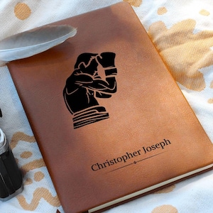 Peut inclure: Un journal en cuir marron avec une silhouette noire de boxeur et le nom "Christopher Joseph" gravé sur le devant.