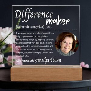 May include: A clear acrylic plaque with the words "Difference maker" and a definition, along with a photo of a smiling woman. The plaque is mounted on a wooden base. The text includes the name "Jennifer Owen".