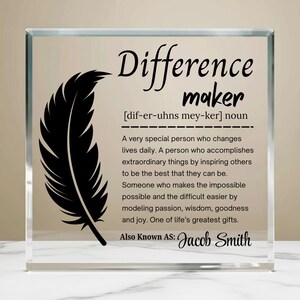 以下が含まれることがあります： 「Difference maker」という言葉と定義が書かれた透明なガラスブロック。左側には黒い羽のグラフィックがあります。「Jacob Smith」という名前が一番下にあります。心のこもった贈り物。