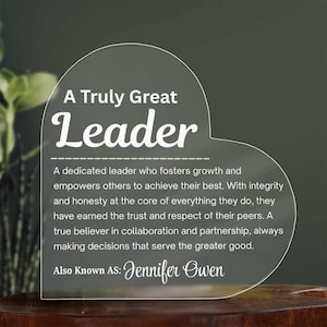 Peut inclure: Plaque en acrylique transparent en forme de cœur avec les mots "A Truly Great Leader" en blanc. La plaque comprend une description d'un leader et le nom "Jennifer Owen".