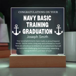 Op de afbeelding: Verlichte acrylplaat met een houten voet. De plaat toont de tekst "CONGRATULATIONS ON YOUR NAVY BASIC TRAINING GRADUATION" en de naam "Joseph Smith". Witte ankers flankeren de tekst. Een felicitatiebericht is ook inbegrepen.