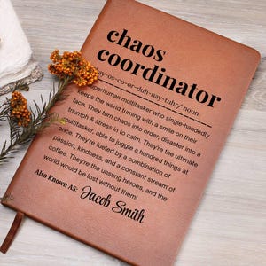 以下が含まれることがあります： 「chaos coordinator」の文字が黒で印刷された茶色の革製ノート。タイトルの下には、カオスコーディネーターの定義が印刷されています。ノートには「Jacob Smith」という名前も含まれています。