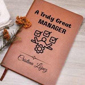 May include: A brown leather journal with the text "A Truly Great MANAGER" and a graphic of a person with checkmarks and a gear. The name "Cristina Lopez" is also printed on the journal.