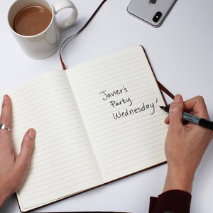 May include: An open notebook with lined pages. The text "Javier's Party Wednesday!" is written in black ink on the right page.
