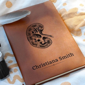 Op de afbeelding: Een bruin lederen dagboek met een vintage illustratie van een nier en de naam Christiana Smith gegraveerd op de voorkant.
