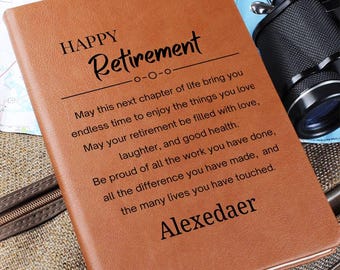 May include: A brown leather-bound journal with the words "HAPPY Retirement" and a personalized name. The journal contains an inspirational message about retirement. A camera is visible in the background.