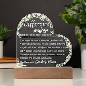 May include: A heart-shaped acrylic plaque with the words "Difference Maker" and a definition, set on a wooden base. The plaque is decorated with floral accents and includes the name "Sarah William".