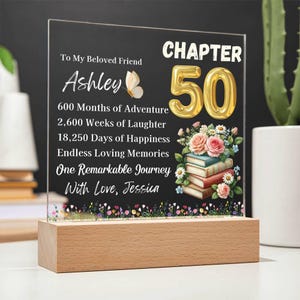 May include: A personalised acrylic plaque with a wooden base. The plaque features the text "Chapter 50" in gold, along with a message to "Ashley" and a floral and book design. The base is made of light-coloured wood.