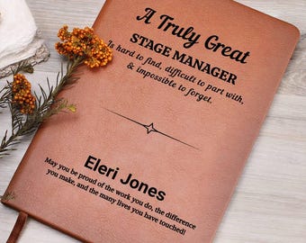 May include: A brown leather journal with the text "A Truly Great STAGE MANAGER" and the name "Eleri Jones". The journal has a ribbon bookmark and is decorated with dried flowers.