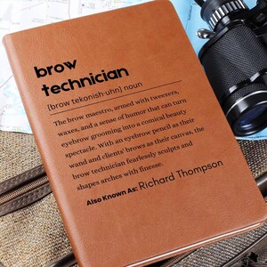 以下が含まれることがあります： 「brow technician」の文字が黒で書かれた茶色の革製ノート。 「brow technician」の定義が下に印刷され、名前「Richard Thompson」も記載されています。 カメラと地図が背景にあります。