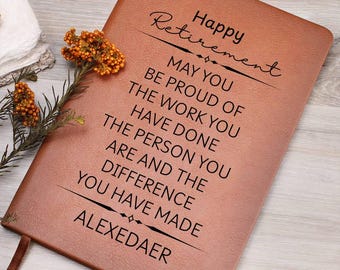 May include: A brown leather journal with the words "Happy Retirement" and a personalized message printed in black. The journal includes a ribbon bookmark and is decorated with a sprig of orange flowers.