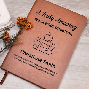 May include: A brown leather journal with the text "A Truly Amazing PRESCHOOL DIRECTOR" and the name "Christiana Smith". The journal has an illustration of books and an apple. A quote is also included.