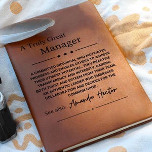 Può includere: Un diario in pelle marrone con il testo "A Truly Great Manager" e una citazione sulla leadership. Il diario è personalizzato con il nome "Amanda Hector".