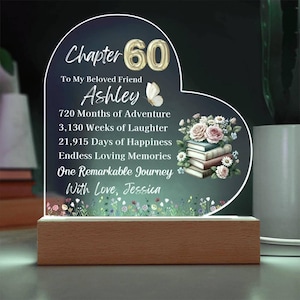 Può includere: Luce notturna a LED a forma di cuore con base in legno. La luce è incisa con le parole "Capitolo 60" e un messaggio personalizzato. Sono presenti anche illustrazioni floreali e di libri.