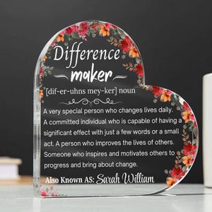 May include: Clear heart-shaped acrylic plaque with floral accents. The plaque features the words "Difference maker" and a definition. The name "Sarah William" is also included. The edges are decorated with red and orange flowers.
