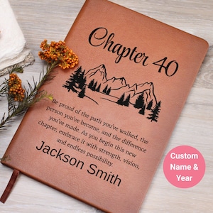 Peut inclure: Un journal en cuir marron avec le texte "Chapitre 40" et un graphique de montagne et d'arbres. Le journal comprend le nom "Jackson Smith" et une citation de motivation. Un cercle rose indique le nom et l'année personnalisés.