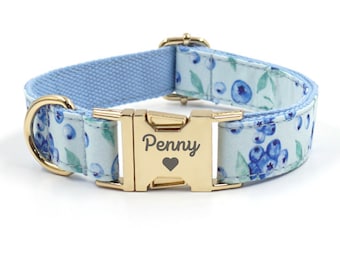 May include: A light blue dog collar with a white and blue blueberry print. The collar has a gold buckle with the name "Penny" engraved on it.