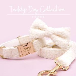 May include: Cream-coloured dog collar, lead, and bow tie set. The collar has a gold-coloured buckle engraved with "CHARLIE" and a phone number. The set is made of a soft, textured material, and the lead has a gold-coloured clasp.