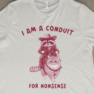 Funny Raccoon Cowboy Riding Cat T-Shirt, I Am a Conduit for Nonsense Shirt, Quirky Graphic Tee, Retro Animal Humor Shirt, Cowboy Cat Tee