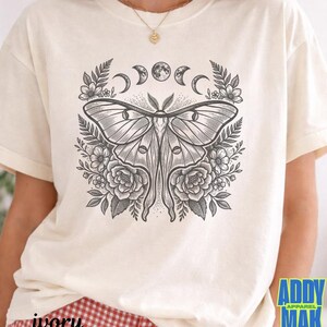 May include: Ivory-colored t-shirt featuring a detailed black and white illustration of a moth with floral and moon phase elements. The text "ivory" is printed at the bottom left. The brand logo "ADDY MAK" is at the bottom right.