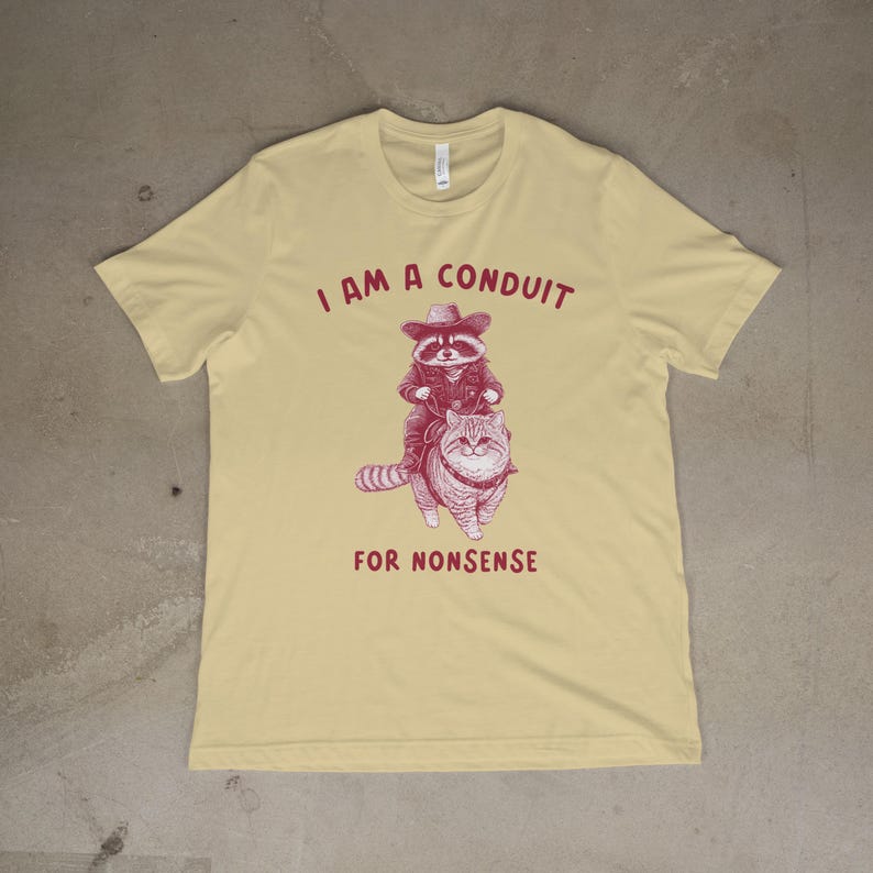 May include: A yellow t-shirt with a red graphic of a raccoon wearing a cowboy hat riding a cat. The text "I am a conduit for nonsense" is printed on the shirt.