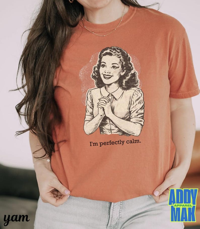 Op de afbeelding: Verbrand oranje t-shirt met een vintage illustratie van een vrouw en de tekst "I'm perfectly calm." De afbeelding is in zwart en wit. Het shirt heeft korte mouwen en een ronde hals.