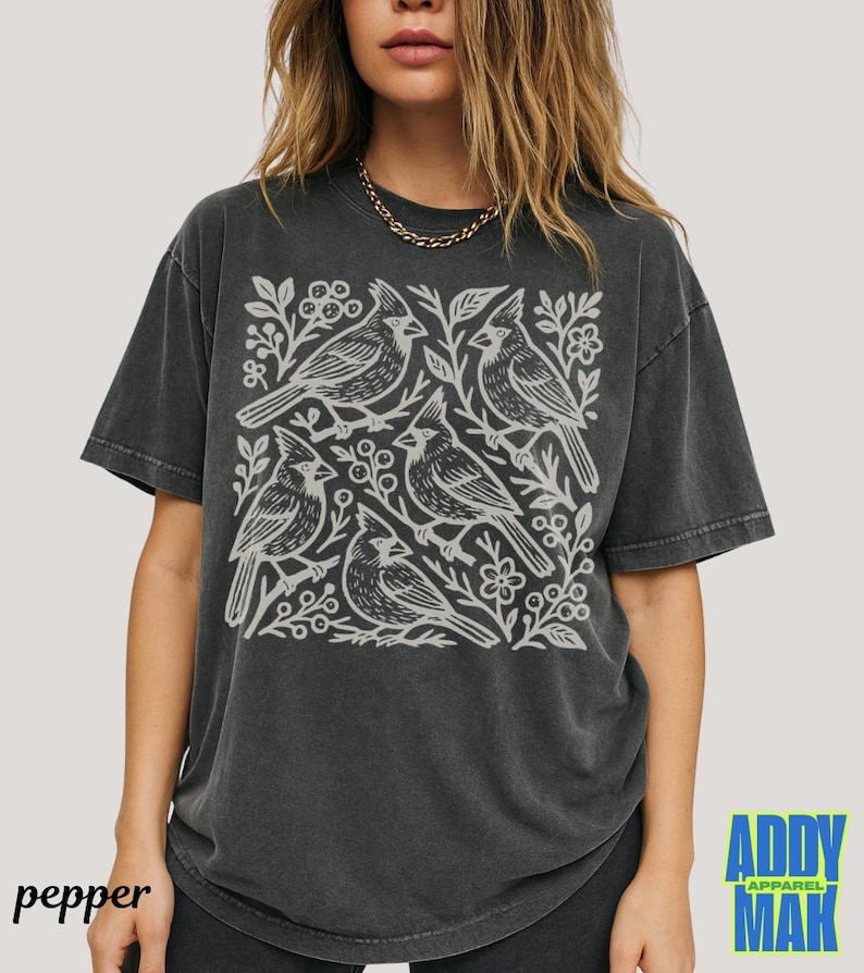 May include: Dark gray t-shirt featuring a white illustration of five birds perched on branches with leaves and berries. The shirt has a vintage, washed look. The word "pepper" is printed on the bottom left. The brand "ADDY MAK APPAREL" is printed on the bottom right.