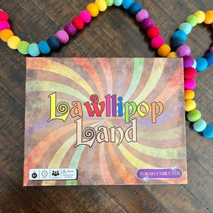 May include: A colorful board game box with the title "Lawllipop Land" and the text "Torah Family Fun". The box has a rainbow swirl design and a warning symbol.