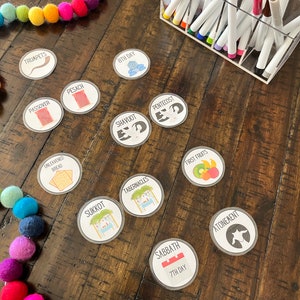 May include: A set of colorful, round, illustrated stickers with Jewish holidays names and symbols. The stickers include Passover, Pesach, Unleavened Bread, Shavuot, Pentecost, Sukkot, Tabernacles, First Fruits, Sabbath, 7th Day, Atonement, and Trumpets. The stickers are on a wooden table with a string of colorful pom-poms.