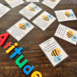 Puede incluir: Un conjunto de diez tarjetas coloridas con una ilustraci&oacute;n de abeja y un vers&iacute;culo b&iacute;blico de Mateo 5. Cada tarjeta tiene un n&uacute;mero del 1 al 10. Las tarjetas est&aacute;n sobre una superficie de madera con letras magn&eacute;ticas de colores que deletrean la palabra "actitudes".