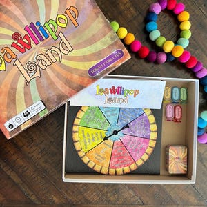 May include: A colorful board game called "LaWllipop Land" for family fun. The game includes a spinning wheel with colorful segments, a game board, and cards. The game is packaged in a box with a colorful design.