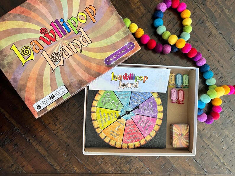May include: A colorful board game called "LaWllipop Land" for family fun. The game includes a spinning wheel with colorful segments, a game board, and cards. The game is packaged in a box with a colorful design.