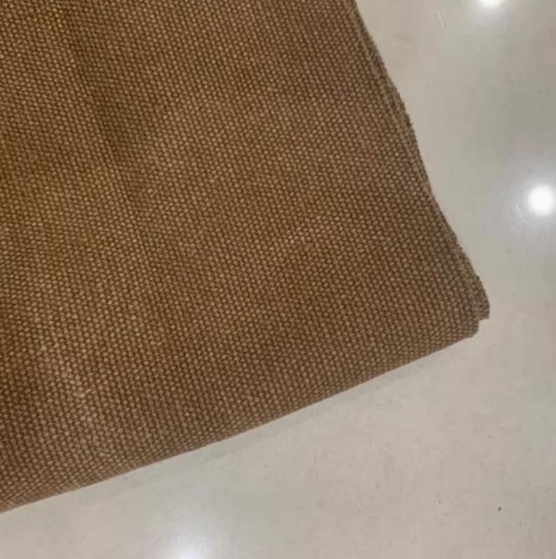 Op de afbeelding: Close-up van een gevouwen, bruine geweven stof. Het materiaal heeft een getextureerde, noppige uitstraling. De stof heeft een warme, neutrale tint, geschikt voor diverse woondecoratie- of knutselprojecten.