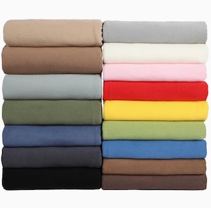 Può includere: Una pila di 10 coperte in pile di diversi colori, tra cui beige, bianco, rosa, rosso, giallo, verde, blu, grigio e nero.