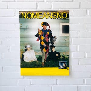 May include: A poster for the band "NO MEANS NO" with a vibrant image of a person in a harlequin costume holding a bucket. Two figures in white and black clothing are in the foreground. The poster has a yellow border.