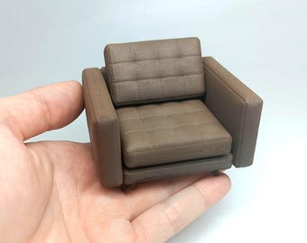 May include: A brown miniature armchair with a tufted back and seat. The armchair is made of a textured material that resembles leather.