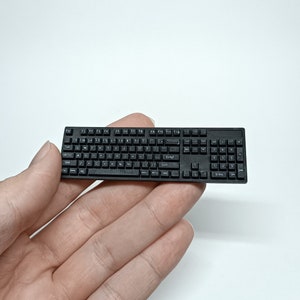 May include: A black miniature keyboard with white lettering. The keyboard has standard keys, including function keys, number keys, and arrow keys. The keyboard is small enough to fit in the palm of a hand.