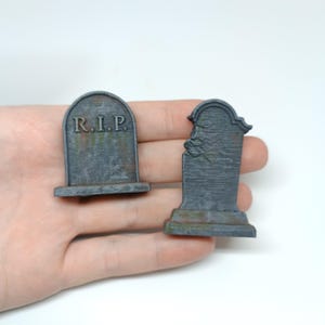 May include: Two miniature gray stone tombstones, one with the inscription "R.I.P." and the other with a chipped top.