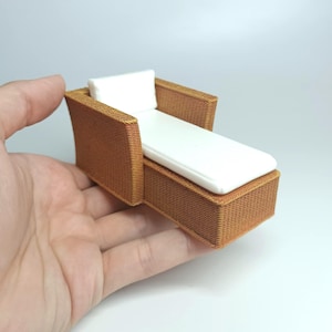 May include: Miniature brown wicker chaise lounge with a white cushion and pillow. The small furniture piece is designed with a woven texture and is perfect for a dollhouse or other small-scale setting.