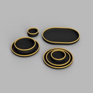 Puede incluir: Un conjunto de fuentes negras para servir con bordes dorados. El juego incluye una bandeja ovalada, varias bandejas redondas y cuencos pequeños. Los artículos están dispuestos sobre una superficie gris, mostrando un diseño moderno.