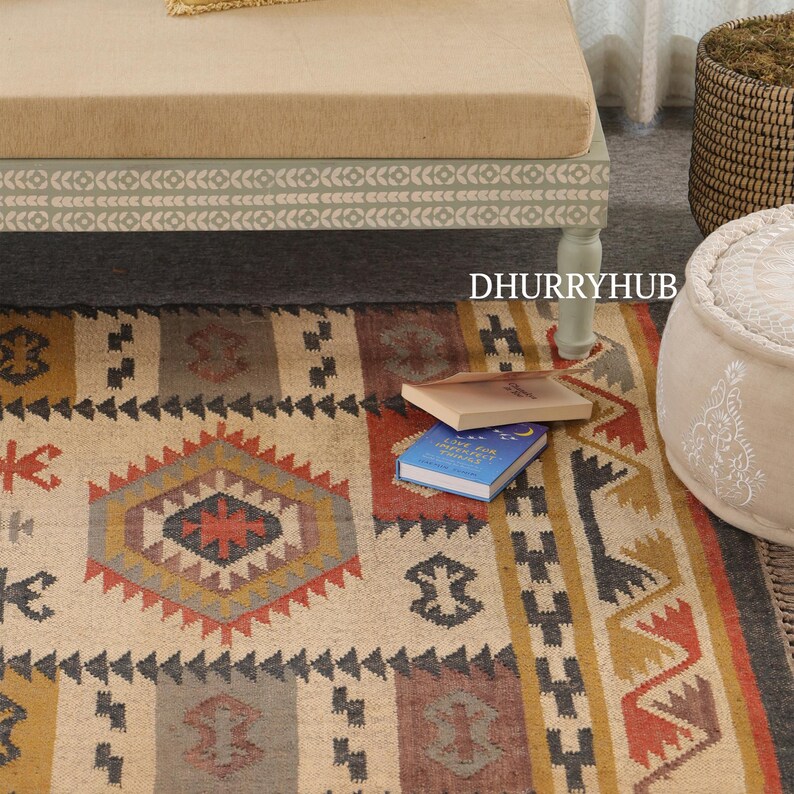 May include: A beige and brown patterned rug with geometric designs. The rug is made of natural fibers and has a rustic look. It is placed on a wooden floor and has a light green bench in the background.