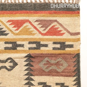 May include: A handwoven rug with a geometric pattern in shades of brown, red, and yellow. The rug has a fringe border and the text "DHURRYHUB" is visible in the top right corner.