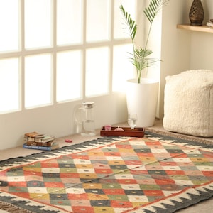 May include: A colourful, geometric patterned rug with a black background and fringe edges. The rug is made of natural fibres and has a hand-woven look.