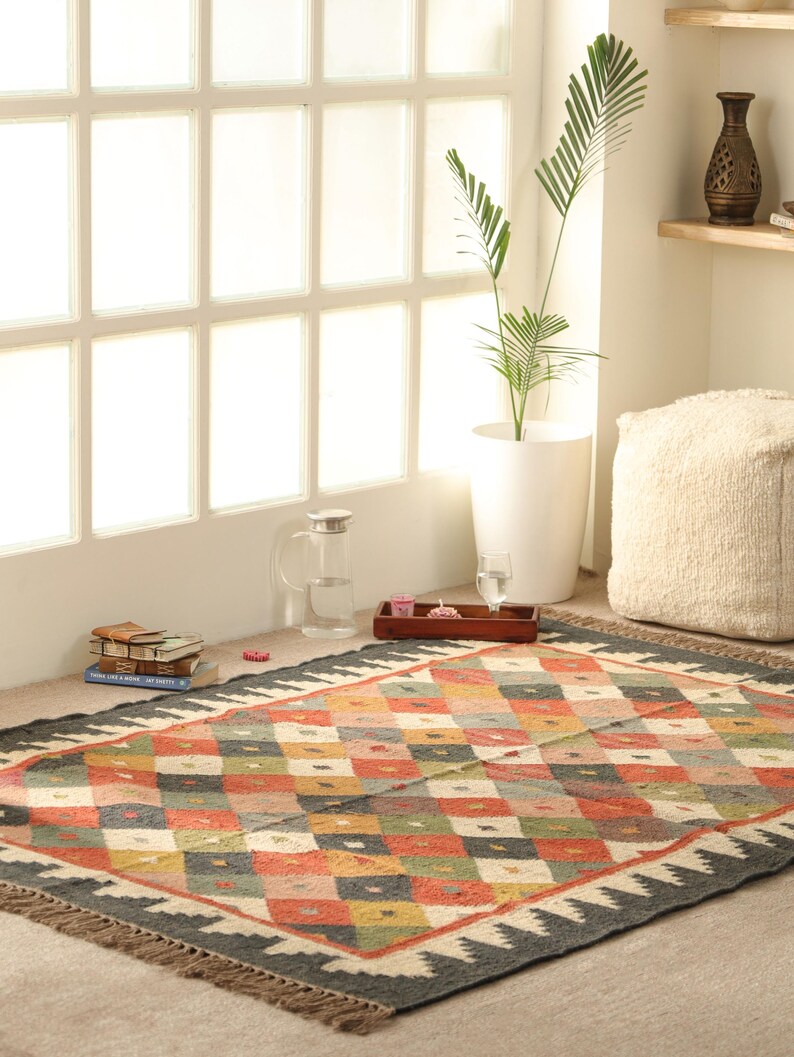 May include: A colourful, geometric patterned rug with a black background and fringe edges. The rug is made of natural fibres and has a hand-woven look.