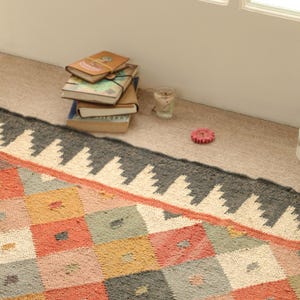 May include: A colourful, geometric patterned rug with a black and white border. The rug is made of woven fabric and has a distressed look.