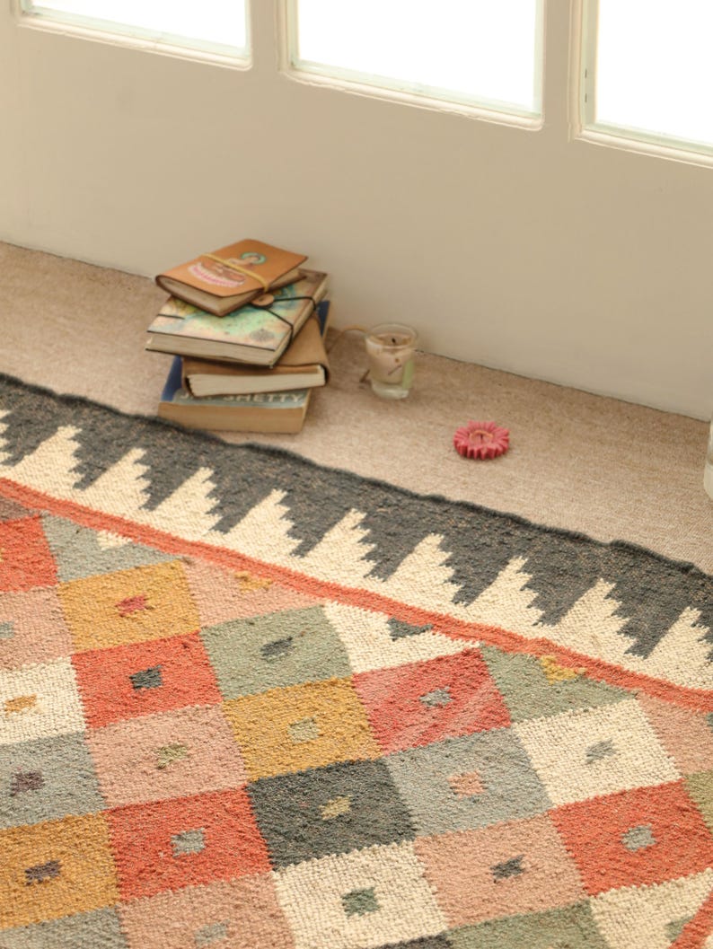 May include: A colourful, geometric patterned rug with a black and white border. The rug is made of woven fabric and has a distressed look.