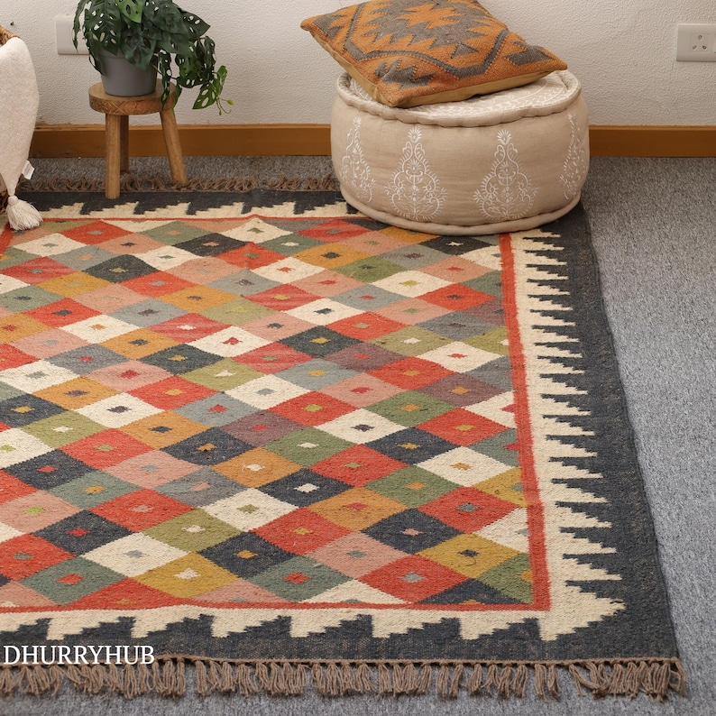 May include: A colourful diamond patterned rug with a black border and fringe. The rug is made of natural fibres and has a rustic, hand-woven look.
