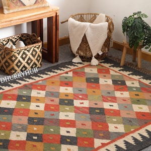 May include: A multicoloured geometric patterned rug with a black border and fringe. The rug is made of natural fibres and has a rustic, hand-woven look.